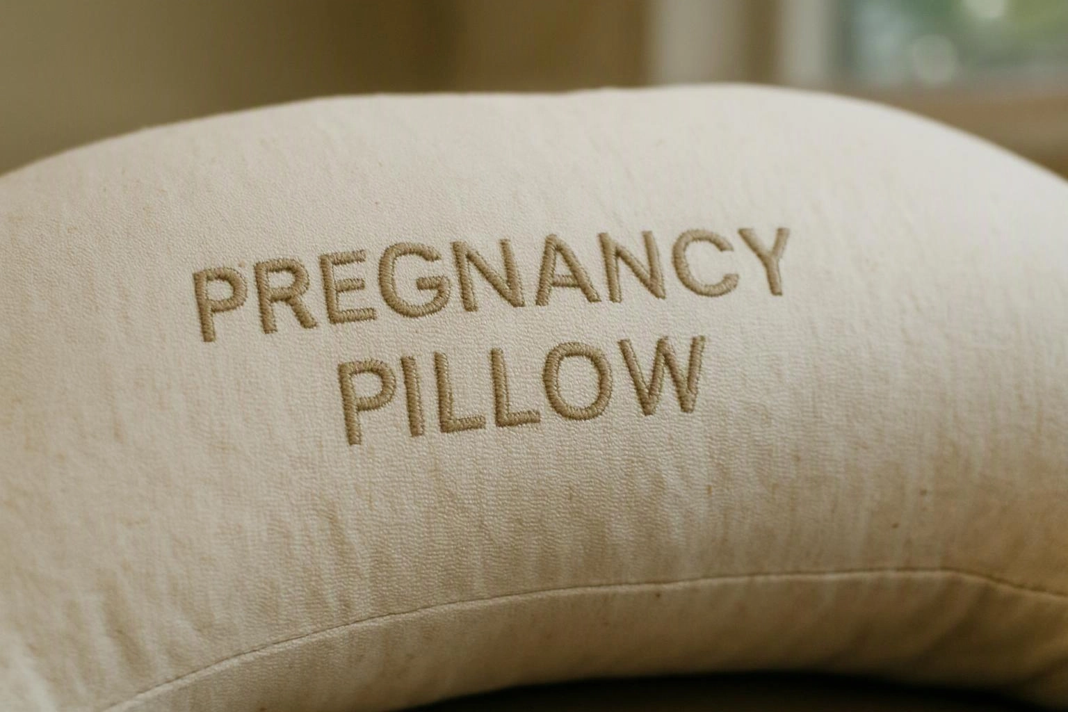 Close-up of a beige pillow embroidered with the words “PREGNANCY PILLOW”