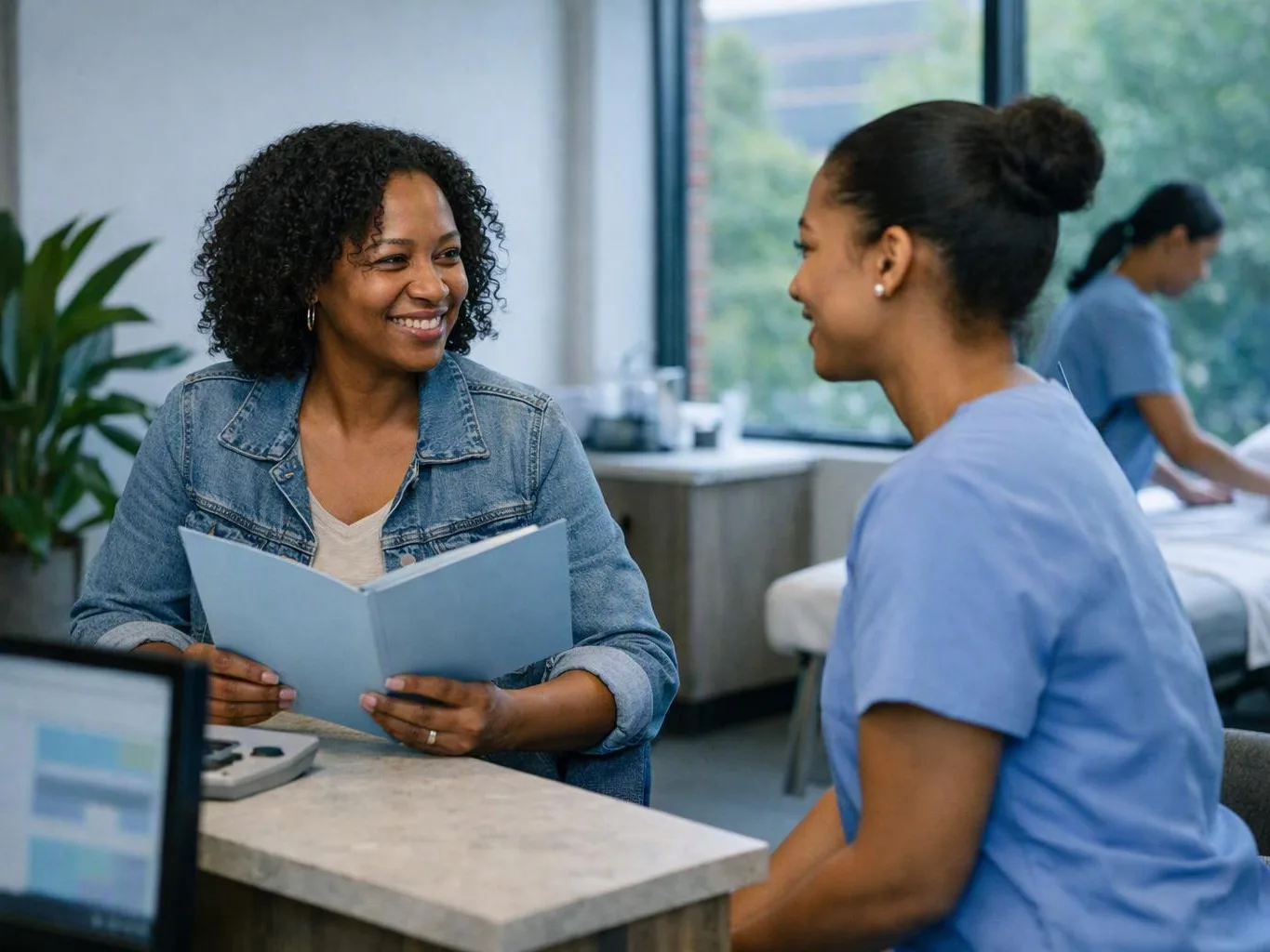 Two women smile and talk across a table in a bright clinic room